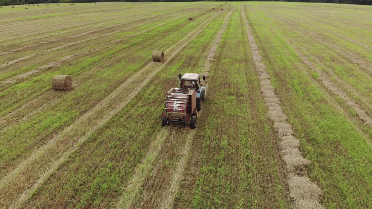 un tractor con una embaladora arrastrada, que produce el embalado de paja en un campo agrícola cosechado