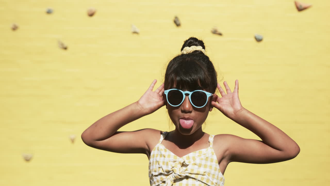 In a school setting, a young biracial student poses playfully, yellow background