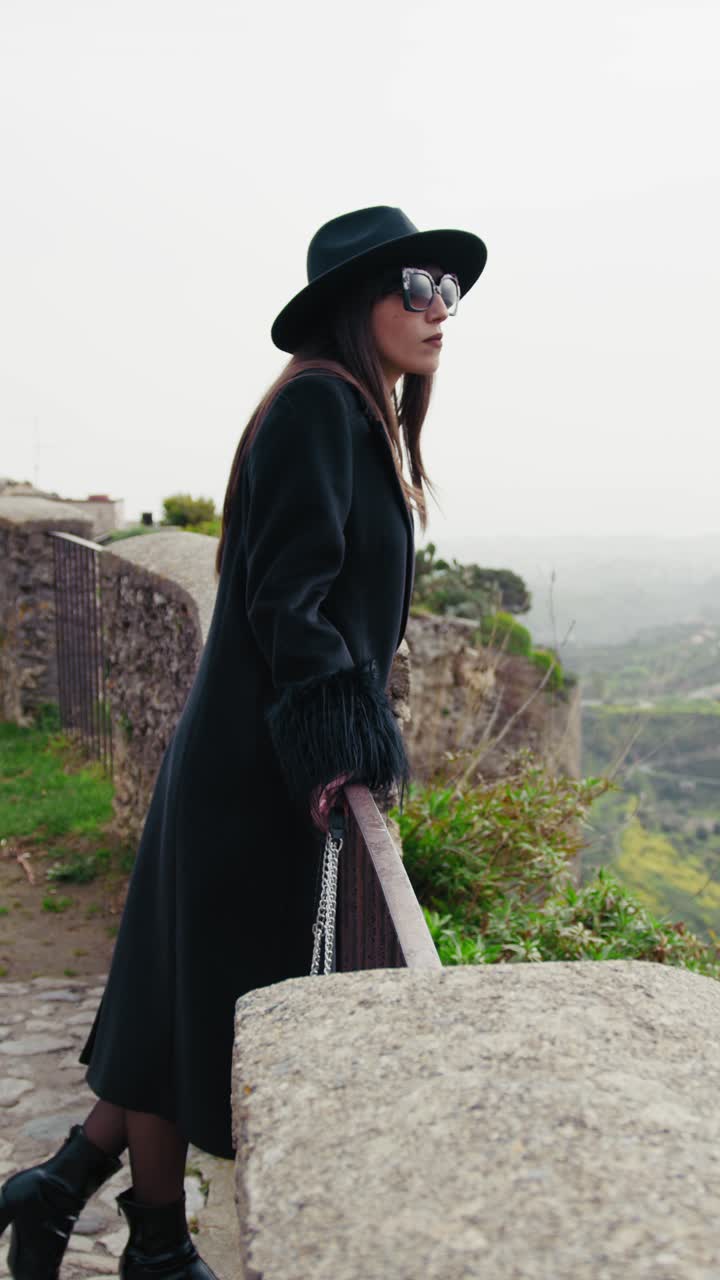 Donna che passeggia e osserva il paesaggio dietro la ringhiera.