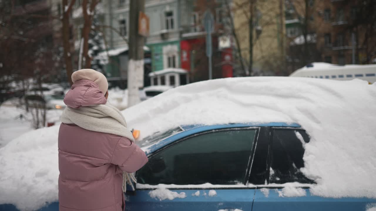 여자 가 겨울 에 차 에서 눈 을 제거 하고 있다