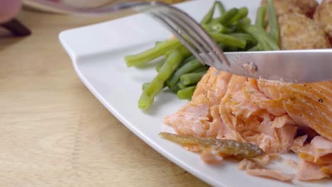 slow motion slider shot of eating a fried salmon fillet on a white plate with vegetables