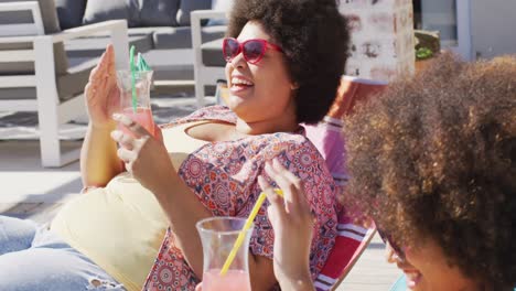 Happy-diverse-female-friends-making-toast-and-smiling-at-swimming-pool-party