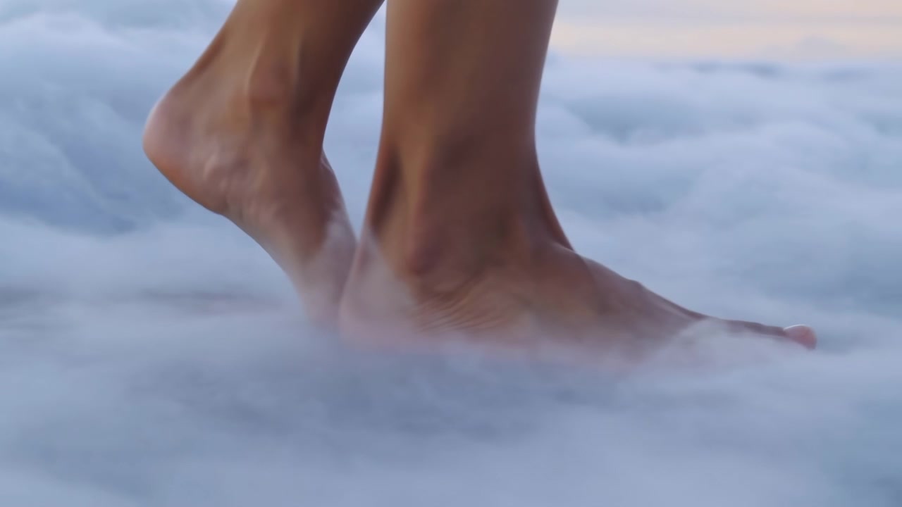 Close view of bare human feet moving across dense cloudlike surface, one foot planted while other lifts at heel, showing gentle weight transfer, soft blur, and tranquil surreal atmosphere