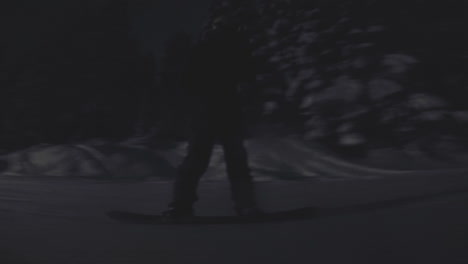silhouetted man snowboards down a mountain at night. lights shine on the snowy park.