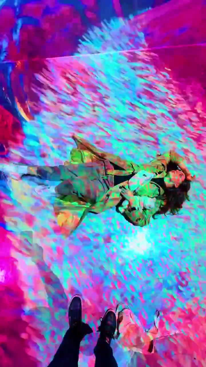 Persona sdraiata in una sala di installazione di arte digitale immersiva. Vivaci motivi astratti rossi e blu proiettati sulla persona e sul pavimento in una mostra d'arte immersiva a New York.