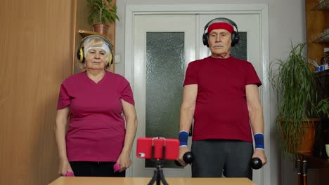 Senior-elderly-couple-watching-online-workout-exercises-on-mobile-phone-and-training-with-dumbbells