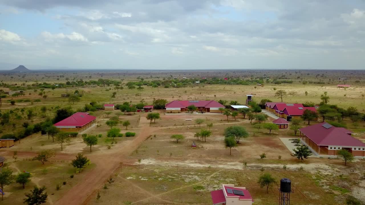 Expansive aerial view showcasing a vocational school in rural Uganda. Surrounded by vast open landscapes and sparse vegetation. Highlighting the serene and remote setting of the educational facility