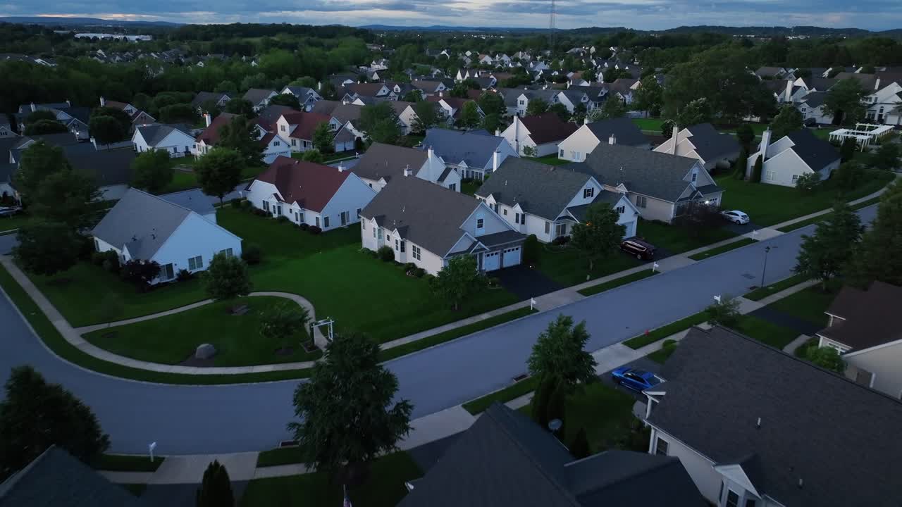 Aerial flyover american housing area in quiet suburbia. Wide shot. Cloudy day in the evening. Single family houses with white facade and different colored roofs. Upper class residential area in USA.