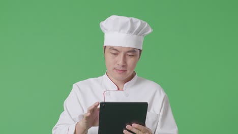 chef asiático usando una tableta mientras camina en el estudio de fondo de la pantalla verde
