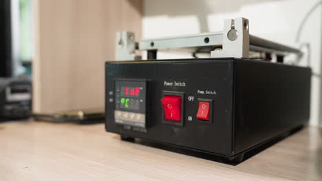 a close-up view of a technician's gloved hand pressing the red power switch on a black temperature control device