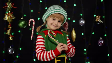 Kid-girl-in-Christmas-elf-Santa-Claus-helper-costume-licking-candy-cane-lollipop-caramel-sweets