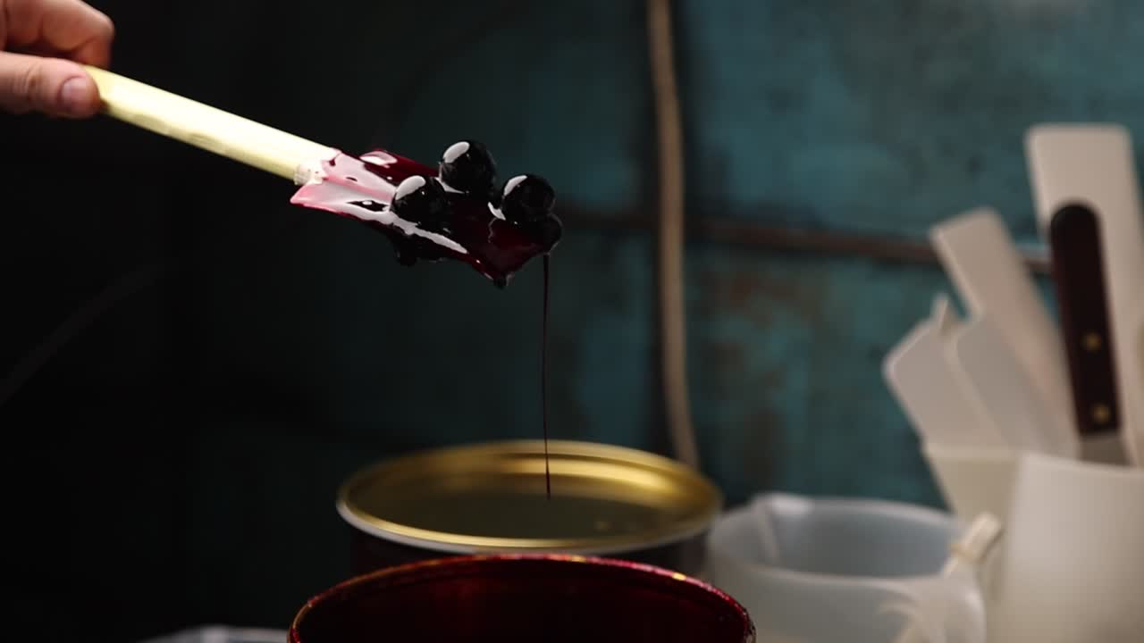 Nærbillede af hånd, der løfter kirsebær i sirup med en spatel