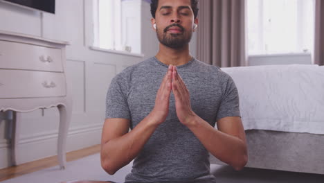 man sitting on yoga mat in bedroom at home wearing wireless earphones and streaming from mobile phone - shot in slow motion