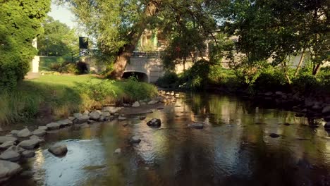 Scenic-river,-surrounded-by-green-trees-in-downtown-Lake-Orion,-MI,-at-the-park,-with-rocks-and-stones-outdoors-in-the-summer