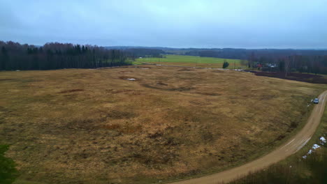 Drone-flying-forward-over-an-empty-open-field,-big-forest-in-the-background