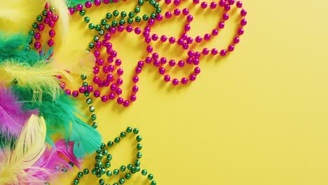 video of pink and green mardi gras carnival beads and feathers on yellow background with copy space