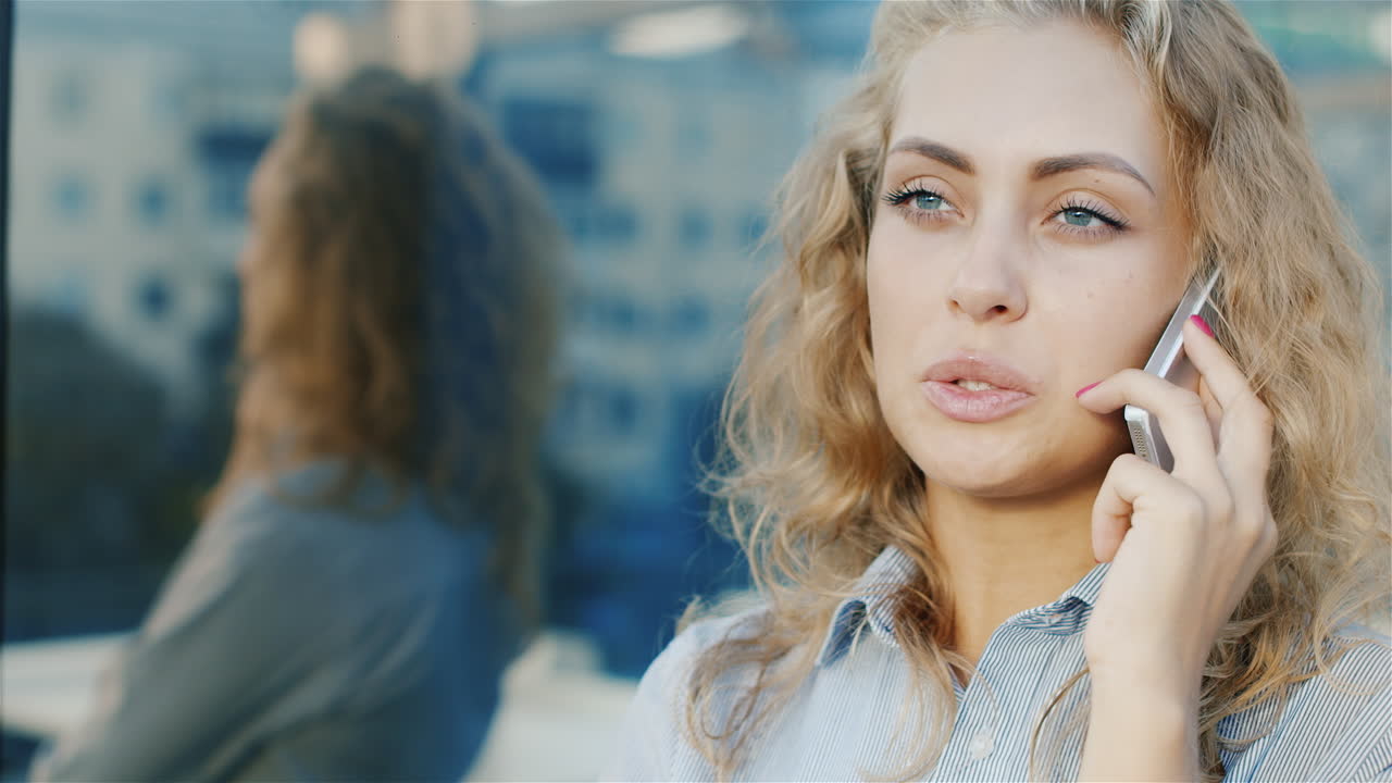 Giovane donna che parla al telefono. Ritratto in città, in un ambiente moderno con pareti di vetro.