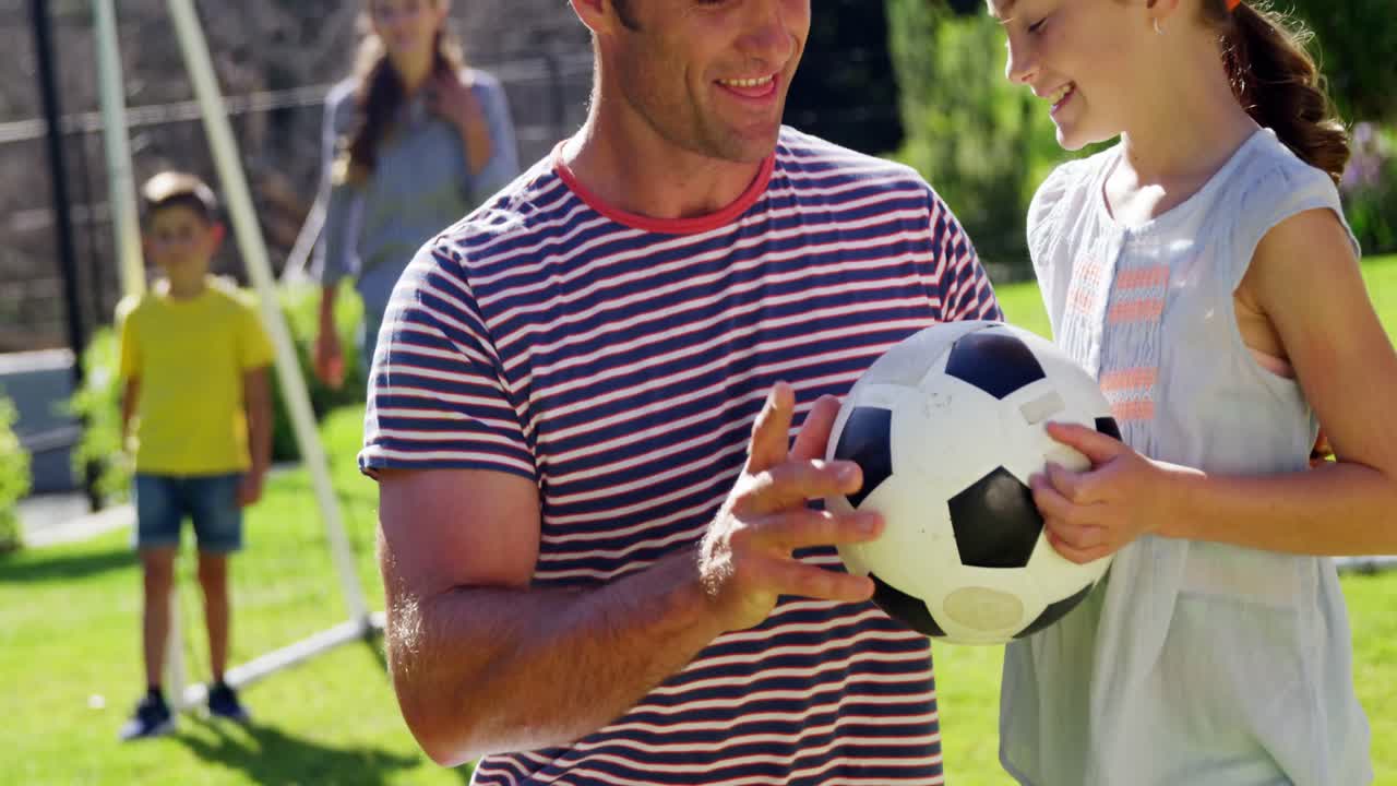 padre ayudando a su hija a jugar al fútbol