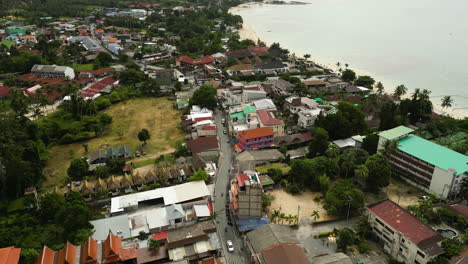 aerial flyover tourist town in koh tao thailand with traffic on main road during cloudy day