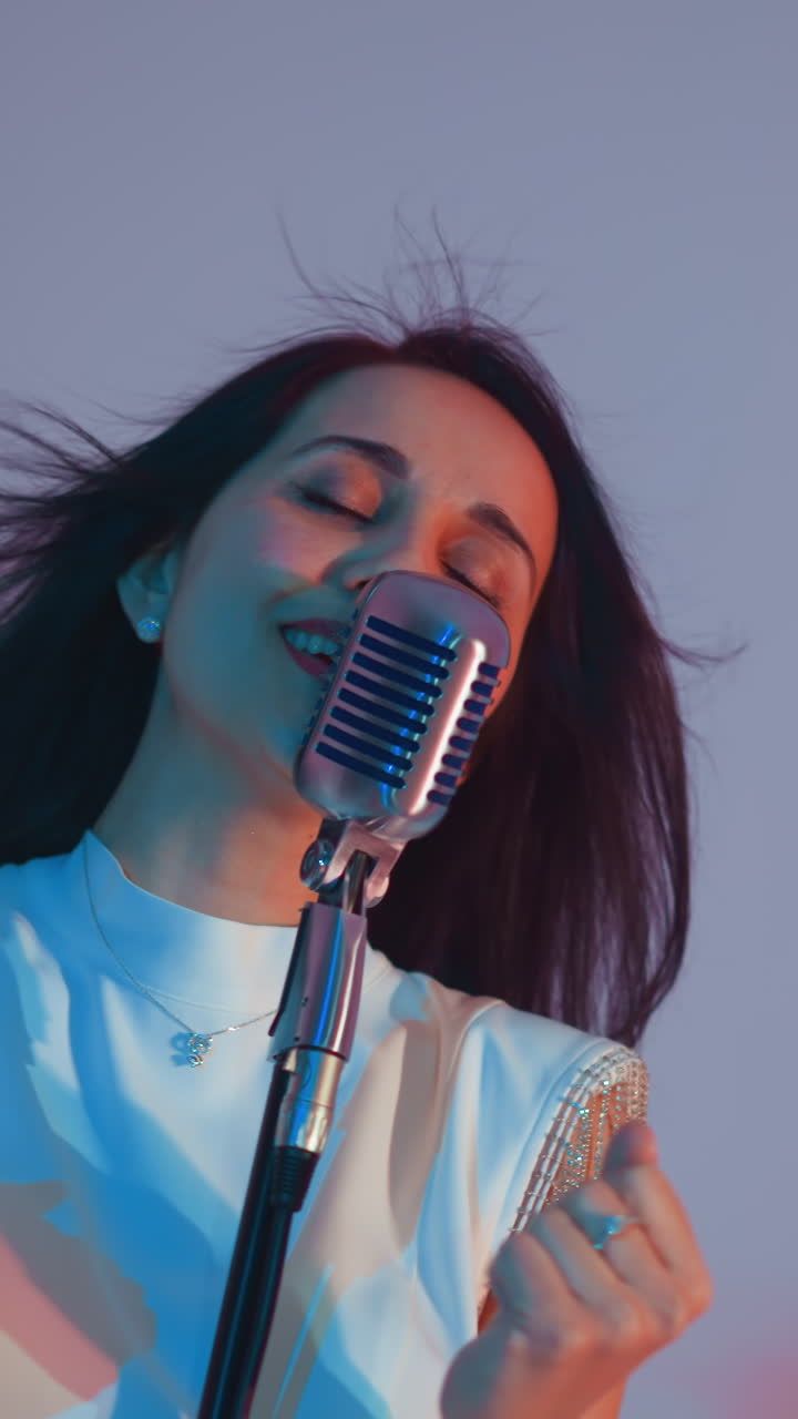 하 옷을 입은 가수가 열정적으로 연주하고, 손을 고 눈을 감고 깊은 감정을 표현하고, 그녀의 머리카락은 분홍색과 파란색의 부드러운 배경에 흐르고 있습니다.