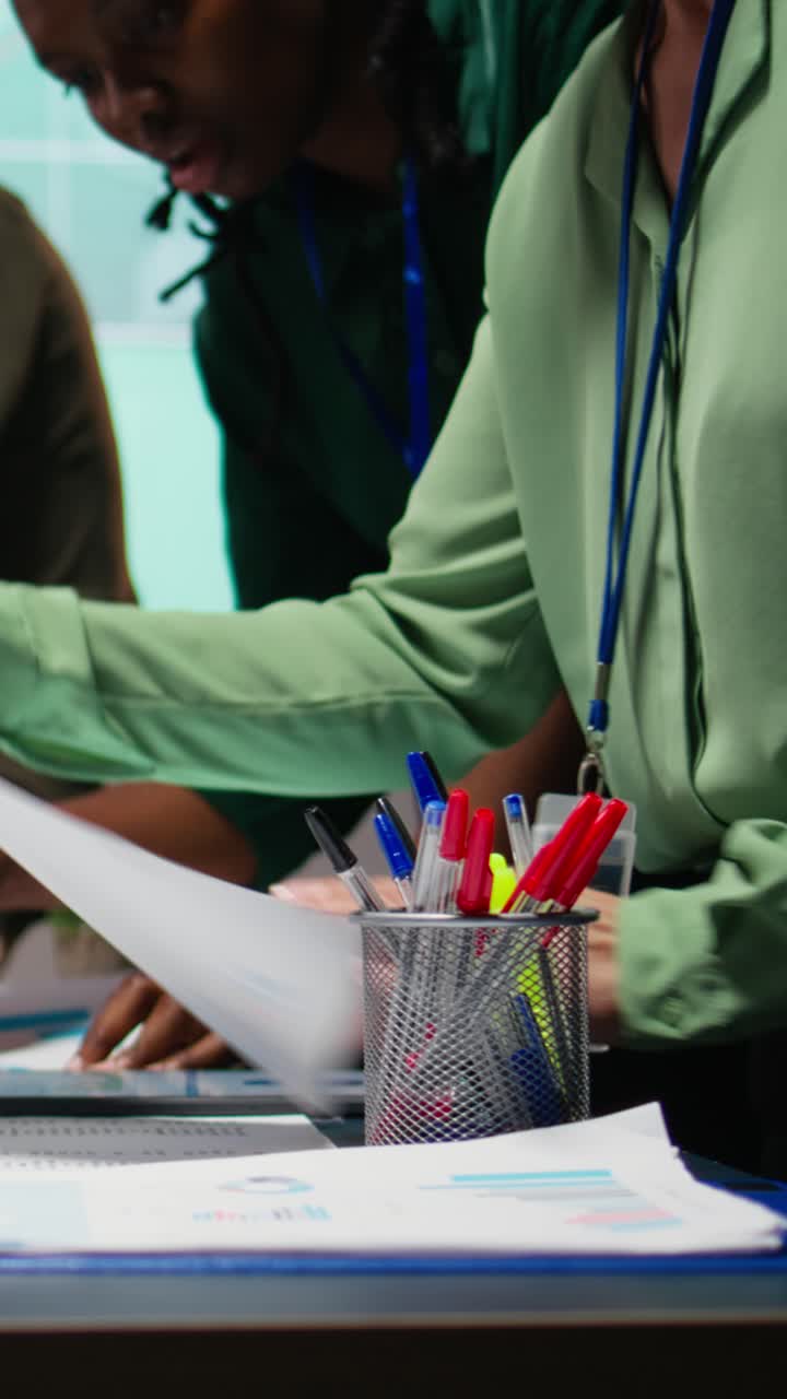 Vertical Video Multiethnic forecasting team reviewing report files during important meeting
