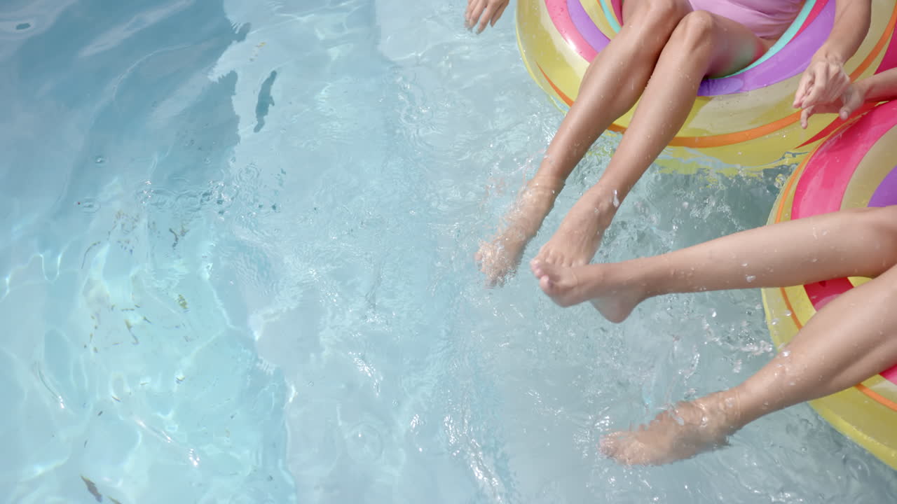 Two girls relaxing in home pool, splashing water with feet on float, copy space