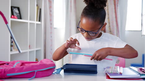 young girl wearing glasses packing bag for school in bedroom