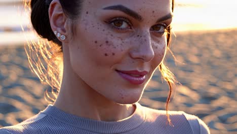 freckled model smiling serenely on a beach during sunset, basking in the warm glow of golden hour light, embodying a sense of peace and happiness in a picturesque outdoor setting
