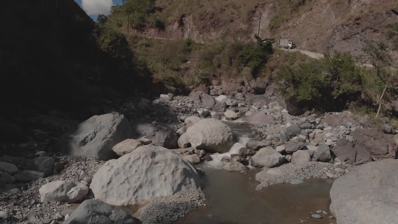 río rocoso que serpentea a través de las montañas en el valle del cañón agua que fluye acercándose rocas grises árboles verdes cielo azul y nubes antena lenta avance suave proximidad al pájaro que vuela a través