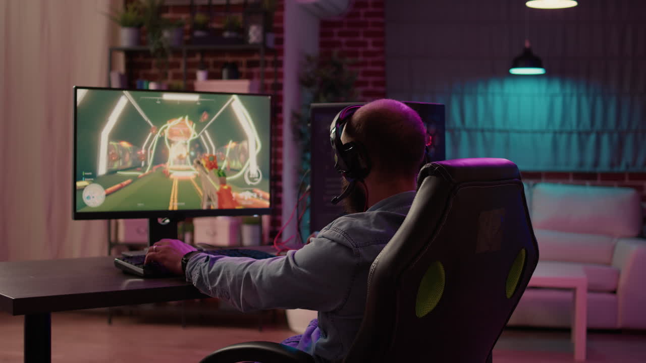 Over shoulder view of man playing online action game congratulates team on headset after celebrating victory