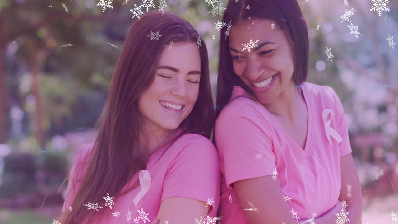 Two women in pink shirts smiling with snowflake animation overlay