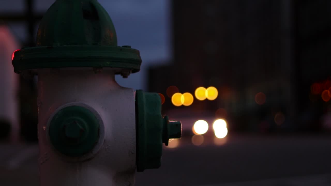Close up of green and white fire hydrant on a street corner. Cars drive by in the background.