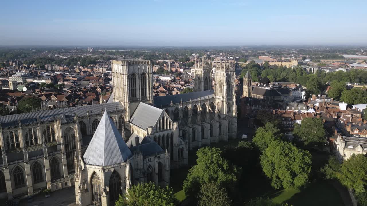 Aerial drone video tracking right to left across York Minster at sunrise, showing the iconic Gothic cathedral illuminated by early morning light in York, England