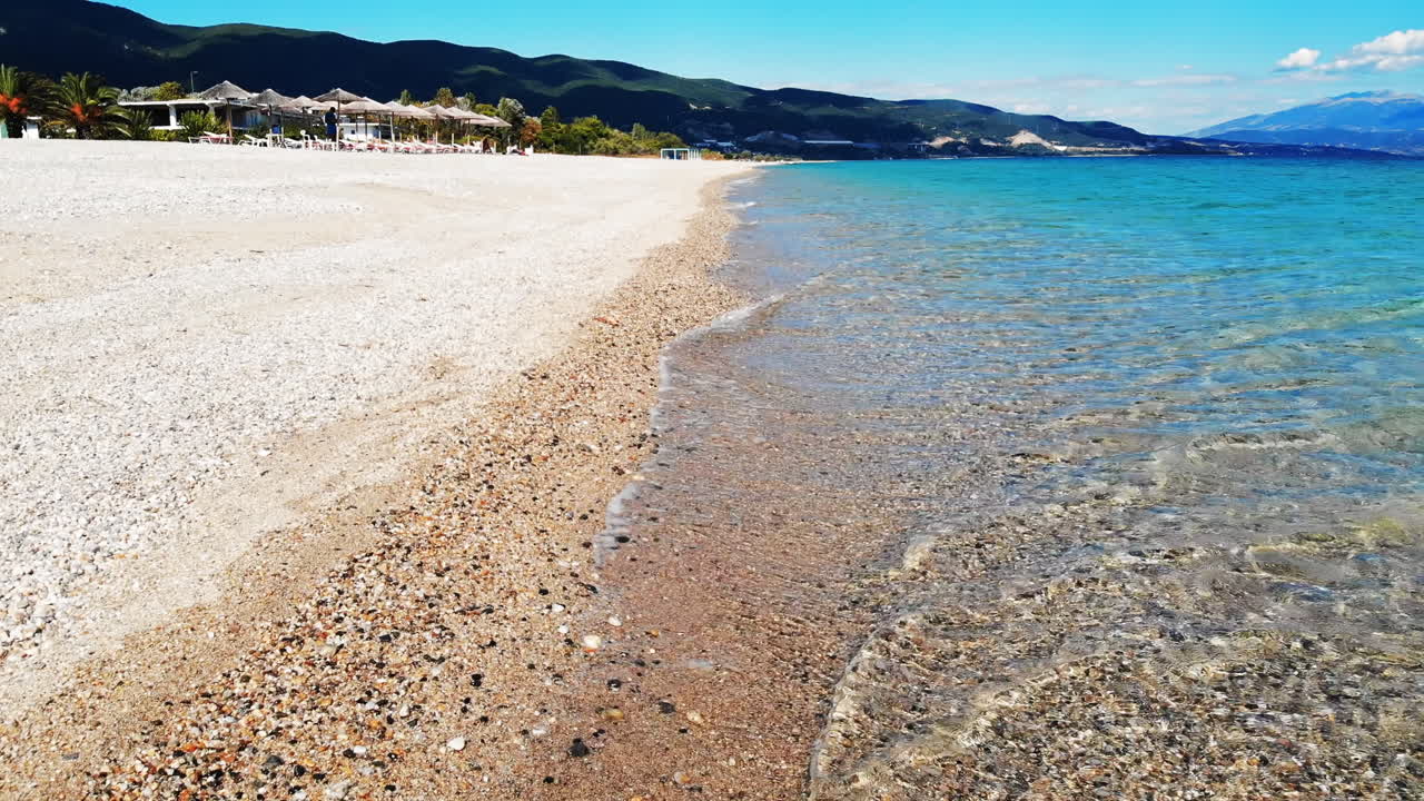 Panorama of the Asprovalta located on the Aegean sea coast with buildings and greenery, green hills. Long beach along the town. Sunny day, view from the drone. Greece