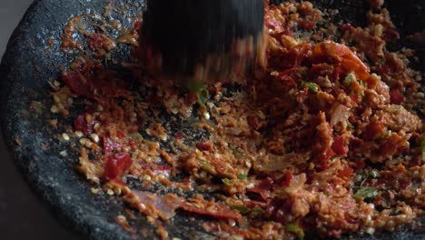 moler a mano chiles rojos y verdes, ajo y cebolla en mortero de piedra, chef preparando salsa de chile picante tradicional indonesia