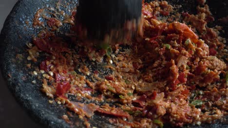 hand grinding red and green chilies, garlic and onion in stone mortar, chef preparing indonesian traditional spicy hot chili sauce