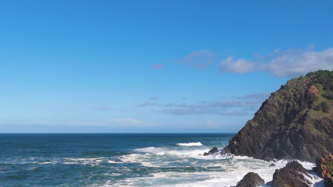 Dynamic ocean waves crash against rocky cliffs under a clear blue sky at Byron Bay, Australia. Captured in vibrant daylight