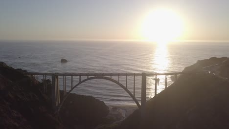 aerial drone shot of bixby bridge with sun and ocean behind