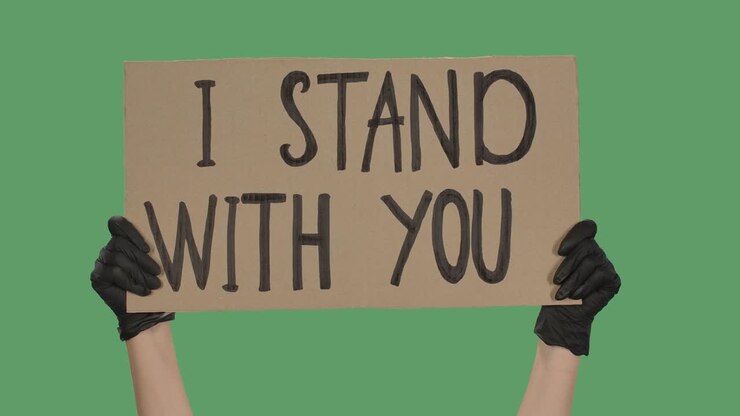Sign I STAND WITH YOU against the background of a green screen, chroma key. Hands in black gloves hold poster from a cardboard box. Close up. Slow motion