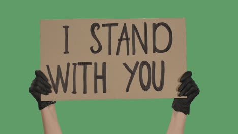 sign i stand with you against the background of a green screen, chroma key. hands in black gloves hold poster from a cardboard box. close up. slow motion