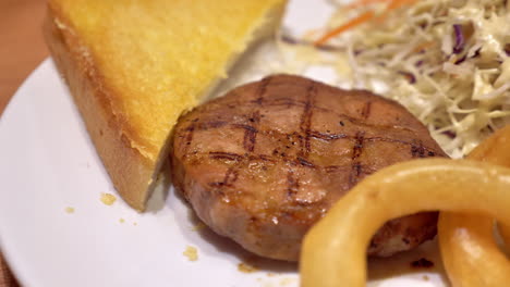 a serving of beef burger steak and side dishes of butted toast, onion rings, and coleslaw salad, served in a restaurant in bankok, thailand