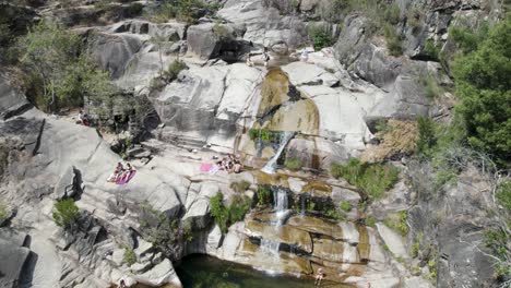 Aerial-top-down-over-people-sunbathing-above-rocks,-at-waterfall-Fecha-de-Barjas