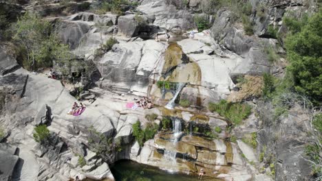 aerial top down over people sunbathing above rocks, at waterfall fecha de barjas