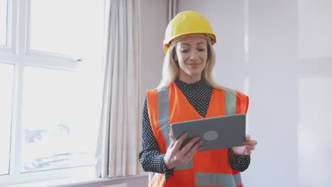 inspector de mujeres con sombrero de blindaje y chaqueta de alta visibilidad con tableta digital realizando una inspección de la casa