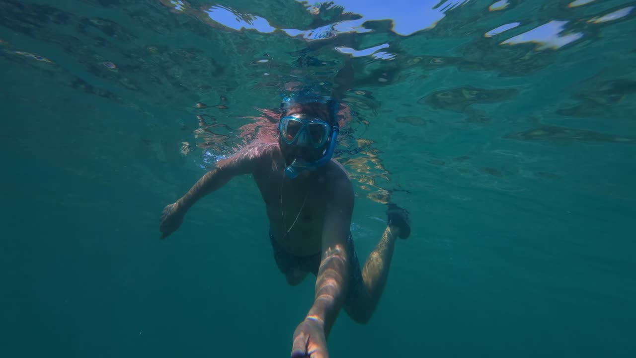 POV submarino de un hombre practicando esnórquel con máscara facial completa y cámara de acción en aguas azules y cristalinas cerca de la playa de Tenacatita, México
