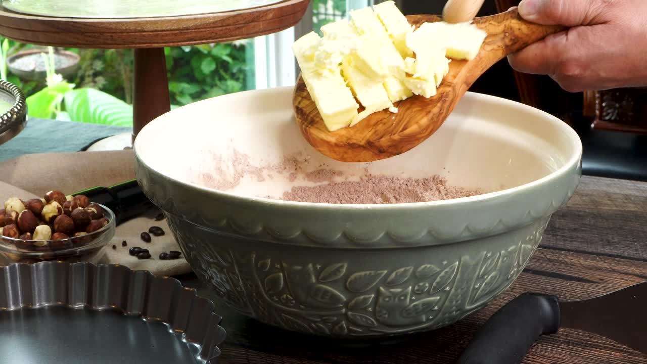 A delicious dessert, Coffee Hazelnut Cream Tart. Made with espresso powder, chocolate crust and loaded with crushed hazelnut. Adding butter to green mixing bowl to make a chocolate batter on a table