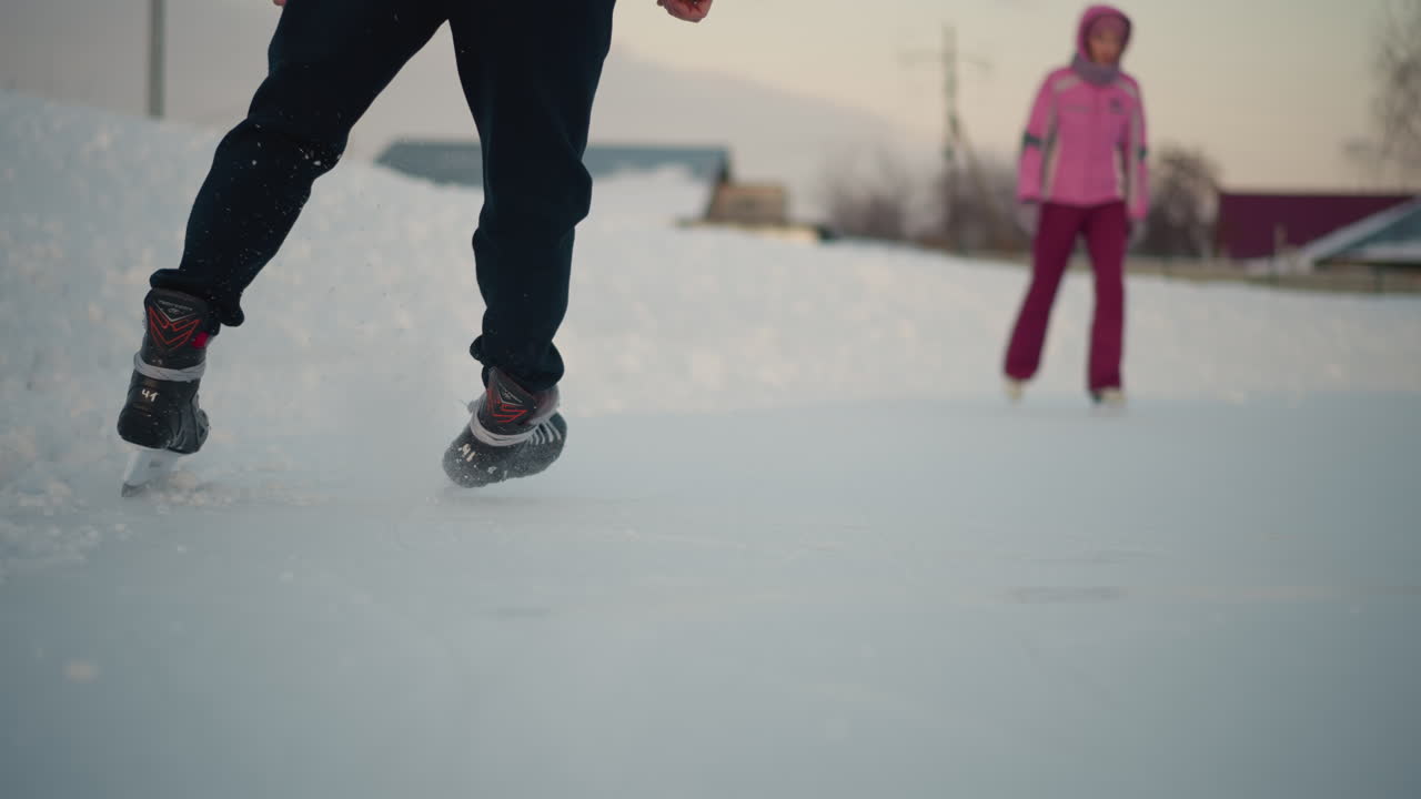 experienced skater skillfully gliding across ice rink with observer watching, blurred buildings in background under soft winter sky with fresh skate tracks visible on smooth surface