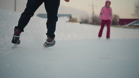 experienced skater skillfully gliding across ice rink with observer watching, blurred buildings in background under soft winter sky with fresh skate tracks visible on smooth surface