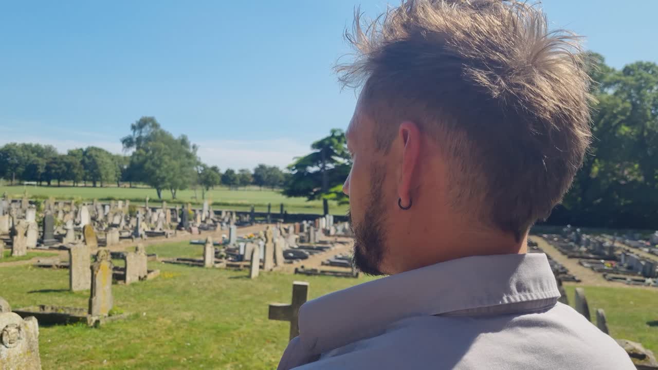Close-up rear view of a man gazing over tombstones in Crowland Abbey cemetery, UK, on a sunny day, deep in thought about life and death
