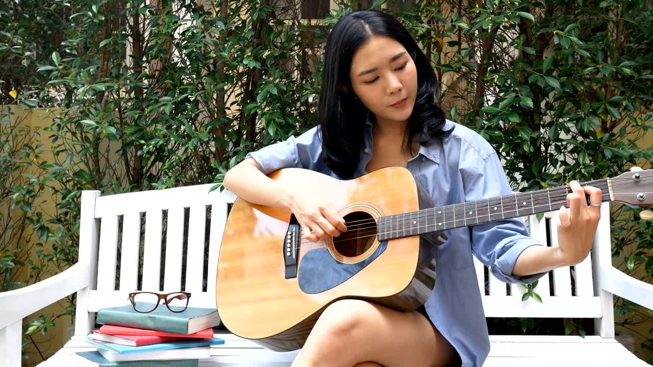 정원에서 미소 짓고 기타를 연주하는 매력적인 아시아 여성.